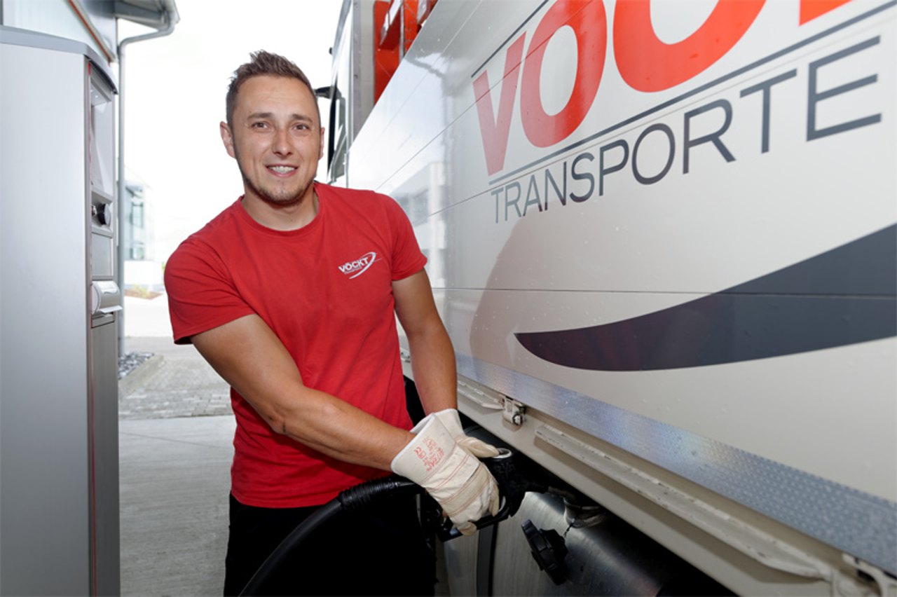 Mann in rotem T-Shirt betankt einen weißen LKW mit "VOGL TRANSPORTE"-Logo.